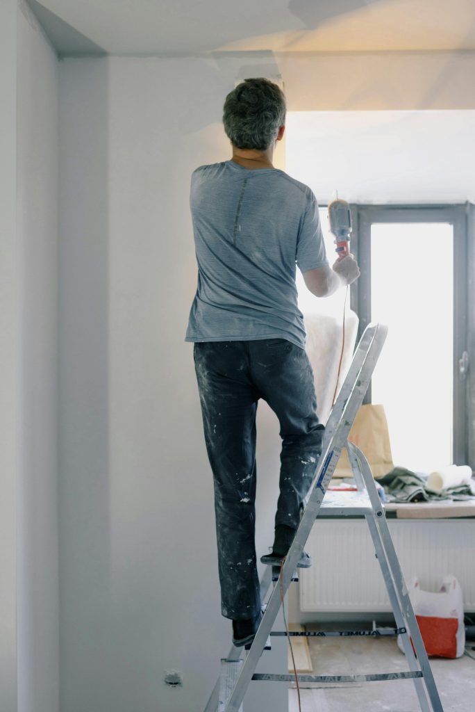 hombre pintando una pared de color blanco, arriba de una escalera